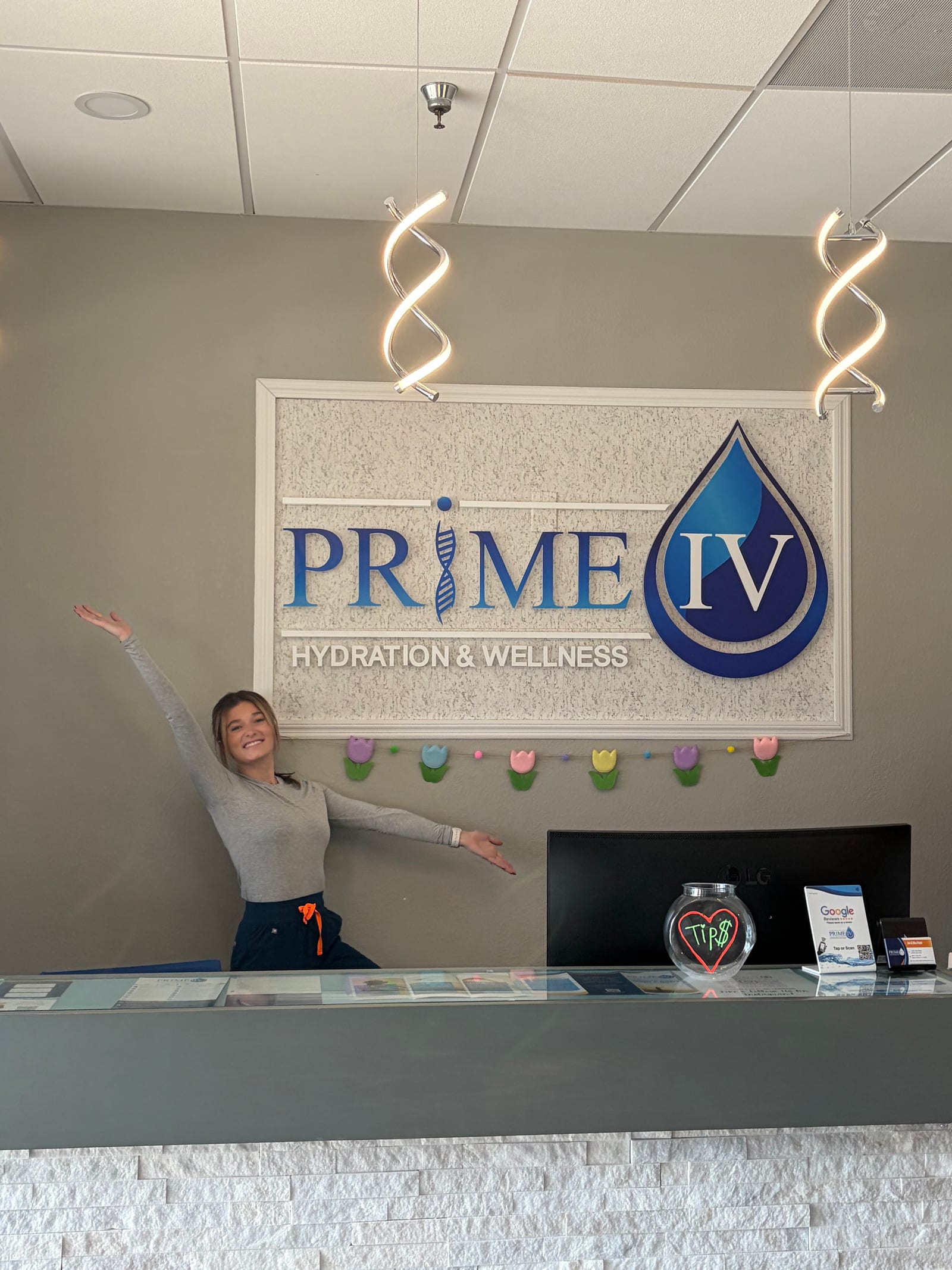 A Prime IV Palm Harbor team member welcoming clients at the front desk beneath the Prime IV Hydration & Wellness sign