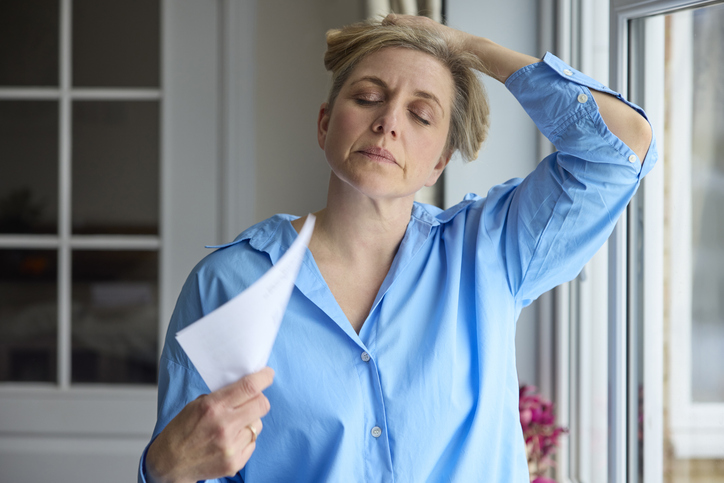 Woman experiencing a hot flash, fanning herself near a window during perimenopause